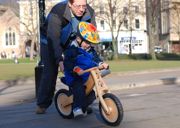 Adult Man Pushing Child On Balance Bike