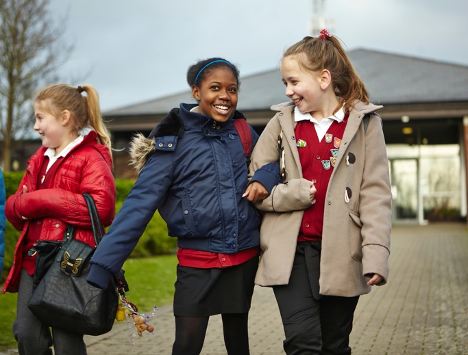 Smiling girls with interlocked arms walking to school